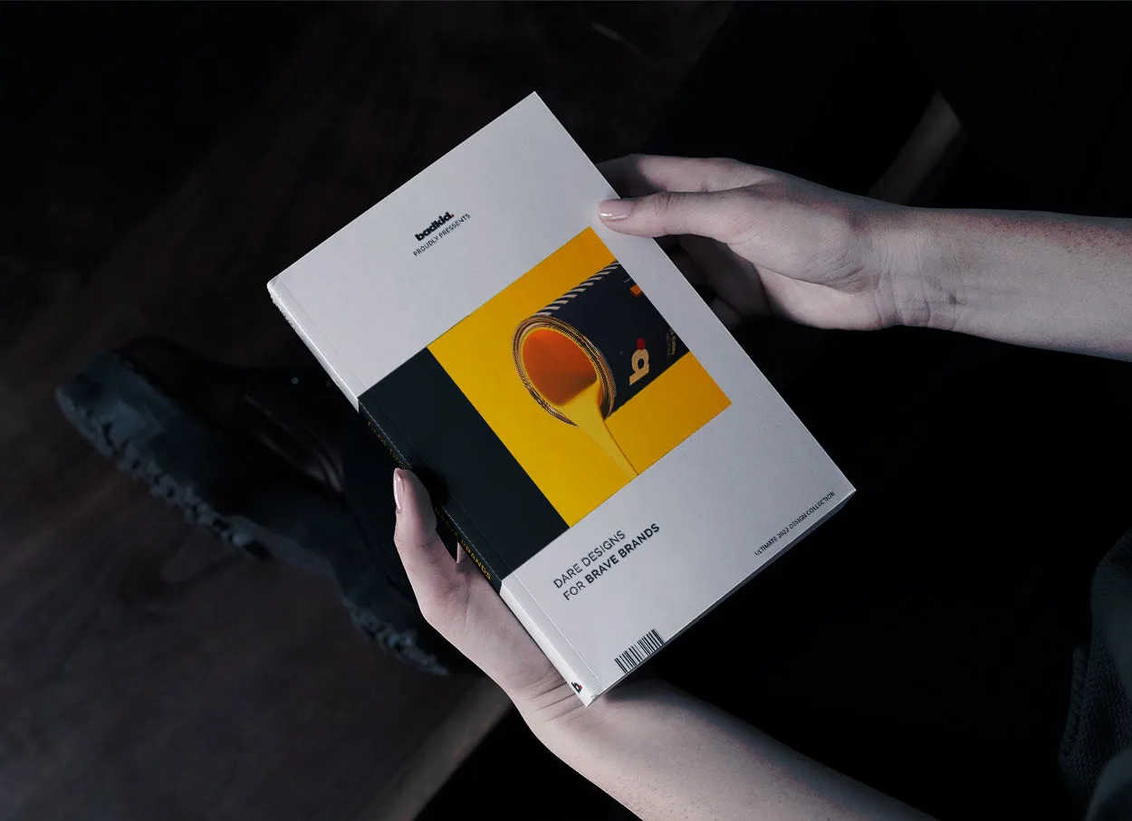 Hands holding a printed badkid design collection with a yellow paint pour on the cover